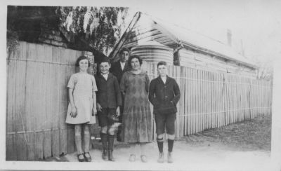 1927 - Mary Carrucan (nee Sweeney) with children at Dalton St Farm Eltham
This photo is taken around 1927 at the family house in Dalton St, Eltham, and shows the old kitchen behind the fence. The picture shows

Back: Ken Carrucan (1916 - 1997)
Front: Betty Carrucan (1915 - 1990), John Carrucan (1913-1976), Mary Carrucan nee Sweeney (1876-1961), Patrick Carrucan (1911-1991)
