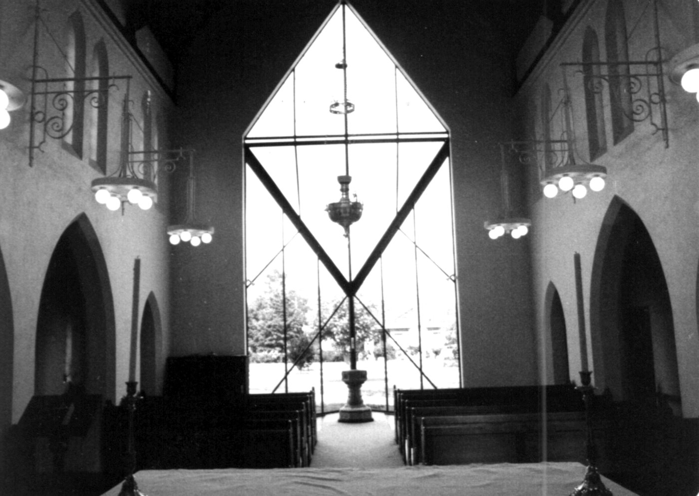 1988 Good Friday 2
The church, as it now stands, is a wonderful example of church architecture. 
The building is notable for its absence of ornamentation and for its lofty, well-proportioned interior. It is the only known example of Heath's church architecture, although he carried out considerable work at Fawkner Crematorium nearby.  
This photo looks towards the eastern end of the church and shows the crossing arch which is filled with a striking steel and glass structure which houses the baptistry,
