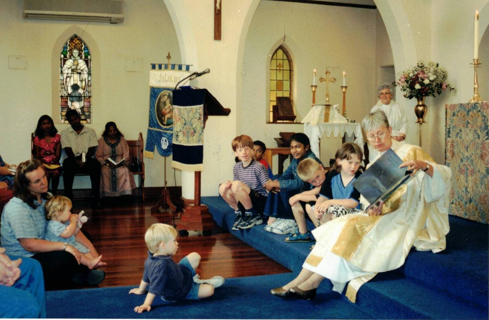 2004 Rev. Willy Maddocks reads a story to the children
Rev. Willy Maddocks was the vicar of St Matthew's Glenroy from 1995 to 2001 and then became the vicar of the newly combined parish of St Matthew's Glenroy with St Linus' Merlynston. Willy had a very active vision of extending the service to include the younger members of the parish. Here she reads a story to the younger congregation members at St Linus during one of her Sunday services.
